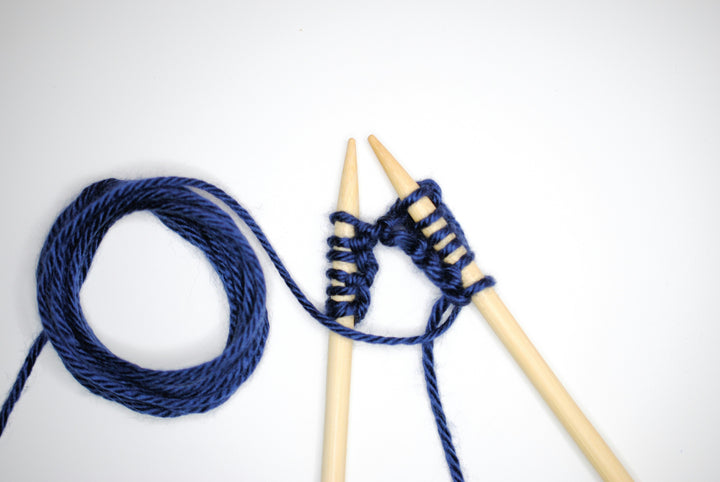 A set of birch knitting needles with blue yarn.